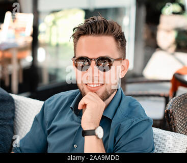 Portrait picture of young man in blue shirt looking at the camera. Handsome businessman wearing sunglasses outdoors. Good looking man smiling Stock Photo