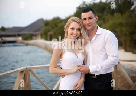 Happy bride and groom smiling and holding hands on a tropical beach of luxury spa resort on Maldives. Wedding and honeymoon on the tropical island. Stock Photo