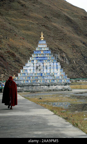 A Buddhist monks walk away from  a Mani pile near Lhagang monastery at Tagong in Sichuan China Stock Photo