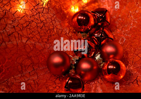 Red Christmas baubles on a transparent red blanket with small lights in the background Stock Photo