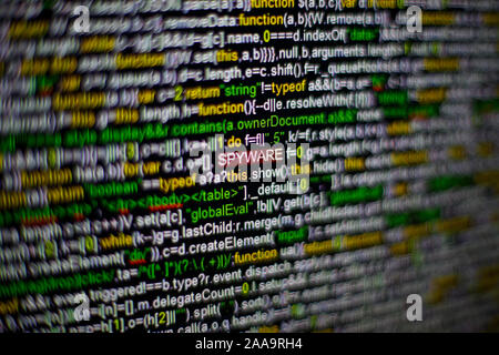 Macro photo of computer screen with program source code and highlighted SPYWARE inscription in the middle. Script on the screen with virus in it Stock Photo