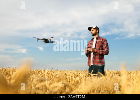 Compact drone hovers in front of farmer with remote controller in his hands. Quadcopter flies near pilot. Agronomist taking aerial photos and videos Stock Photo