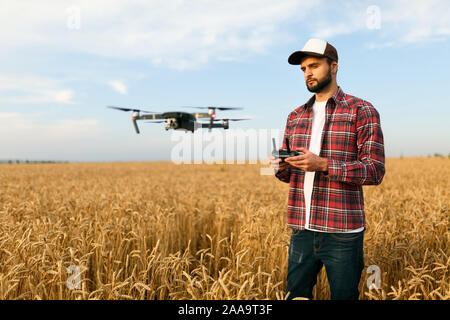 Compact drone hovers in front of farmer with remote controller in his hands. Quadcopter flies near pilot. Agronomist taking aerial photos and videos Stock Photo