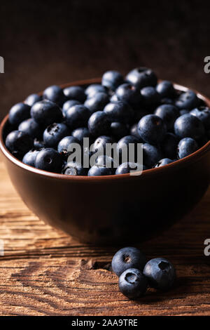Fresh ripe blueberries in brown ceramic bowl on wooden table with dark background, ingredients for healthy diet lifestyle concept, dark and moody Stock Photo