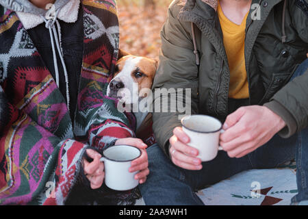 Two people and their funny dog having a lovely time outdoors. Man and woman in warm clothes sit outdoors together with their pet on a lovely chilly da