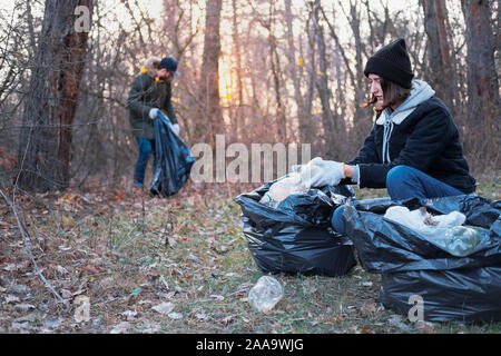 People clean up the forest of plastic trash. Environmental awareness concept: man and woman picking up plastic garbage from the woods while walking or Stock Photo