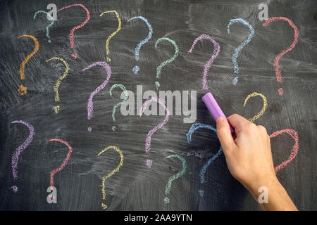 Too many questions. Man drawing colorful question marks on a blackboard. Close up. Stock Photo