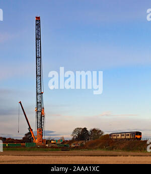 A train passes a giant crane that will be used to replace a railway bridge over the canal. Early morning scene with the moon still in the sky. Stock Photo