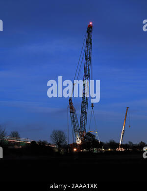 Ainscough’s crane hire built a giant crane next to the railway line at Burscough to replace a bridge over the canal. Scene at dusk as a train passes. Stock Photo
