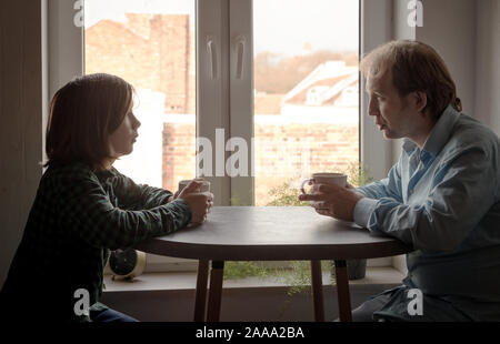 Father and son sitting in the kitchen at the table drinking coffee Stock Photo