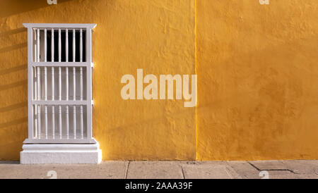 Colonial facade with ocher or yellow wall and window with white balusters, ideal for background, Cartagena de Indias, Colombia Stock Photo