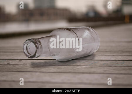 Empty glass bottle lying on wooden boardwalk tossed away. Close up image with selective focus. Stock Photo