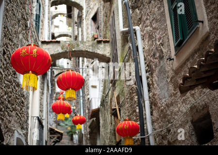 Colorful red and yellow Chinese lanterns decorate a narrow alley in the medieval village of Dolceacqua on the Ligurian coast of Italy. Stock Photo