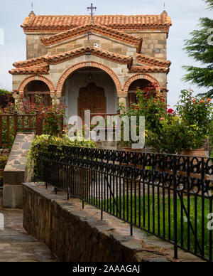 Stone chapel with tile roof surrounded by blooming rose bushes at the Holy Monastery of St. Stephen in Meteora, Greece. Stock Photo