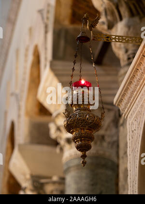 Close up of a hanging brass and red glass candle holder with lit candle hanging in St. Dimitrios Greek Orthodox Church in Thessaloniki, Greece. Stock Photo