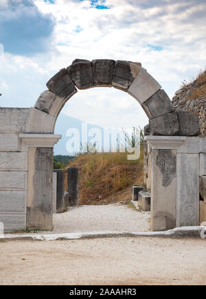 Stone archway with a carved keystone that is part of an ancient gate. Hillside and rock wall are in the background and cloudy skies above. Photographe Stock Photo