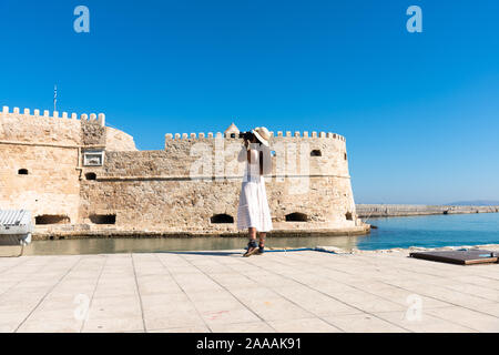 Happy tourist girl on holiday trip to Heraklion, Crete, Greece. Young woman traveller enjoyes sunshine sitting on the dock of Heraklion Venetian port Stock Photo