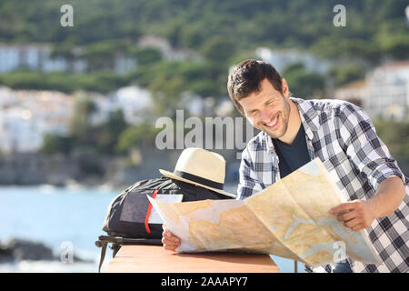 Happy tourist checking map traveling in a coast town on summer vacation Stock Photo