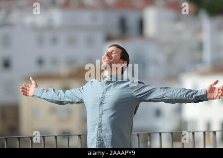 Happy adult man celebrating new day stretching arms standing in a balcony in a rural town Stock Photo
