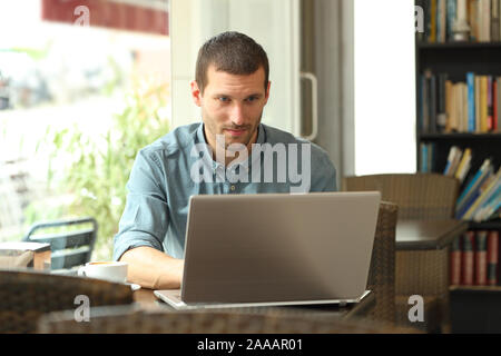 Serious man typing on laptop entering data sitting in a coffee shop Stock Photo