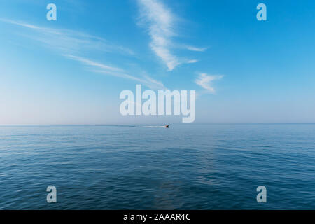 Boat cruising the sea leaving wake on a brilliant sunny day. Beautiful blue sky with light white clouds. Stock Photo