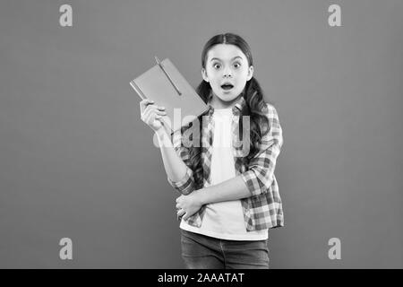 Studying is exciting. Girl cute kid study with book. Interesting book. Did you know. Pupil with work book. Literature and writing lesson. Schoolgirl with notebook doing homework. Learning language. Stock Photo