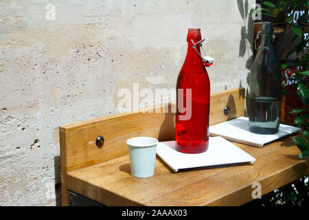 Close-up of a red water bottle and glass on a restaurant table against a light stone wall Stock Photo
