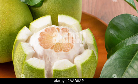 Fresh peeled pomelo, grapefruit, shaddock with green leaves on dark wooden plank table. Seasonal fruit near mid-autumn festival, close up, copy space Stock Photo