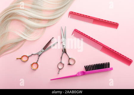 Scissors, combs and other hairdresser's accessories and strand of blonde hair on pink background. Flat lay with space for text. Hairdresser service Stock Photo