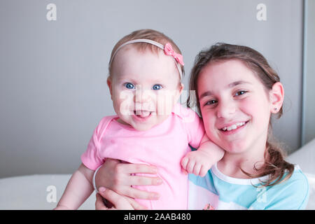 Close up Portrait of Two Sisters, Cute 8 Month Old baby Girl with Big blue Eyes and 8 Years Old School Age Girl With Brown Eyes , Happy Baby Girl Stock Photo