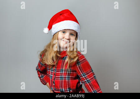 Cute charming little girl in a santa hat and red dress on a gray background. Christmas and new year concept. Stock Photo