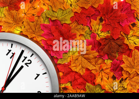 Clock on the colorful autumn maple leaves. Change of season time. Stock Photo