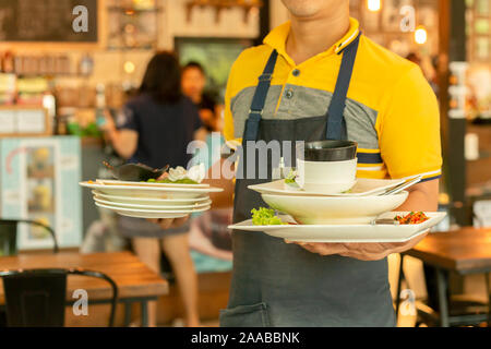 Waiter removing dirty dishes from the tables in restaurant. Stock Photo