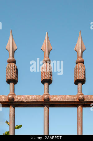 wrought iron spear like spikes on a fence on a blue sky background Stock Photo