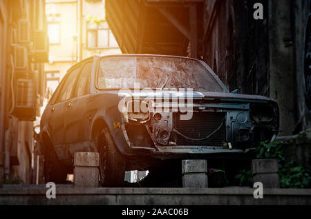 An old abandoned broken and rusty blue car without headlights and a crack on the windshield Stock Photo