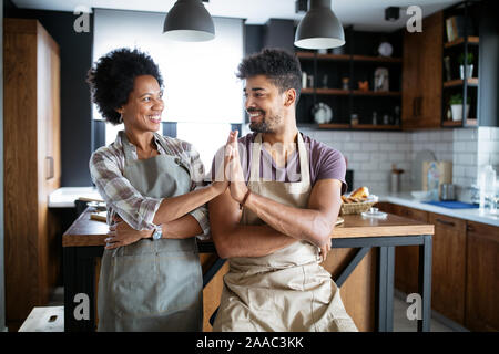 Young happy couple in aprons giving high five in kitchen Stock Photo
