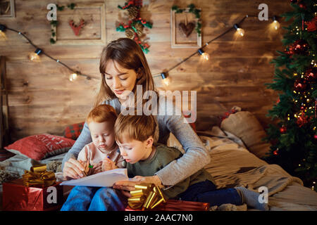 Mother with children watching giftson the bed in Christmas. Stock Photo