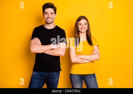 Photo of cheerful cute pretty nice couple with hands folded wearing jeans denim black t-shirt coworking standing confidently isolated over vivid Stock Photo