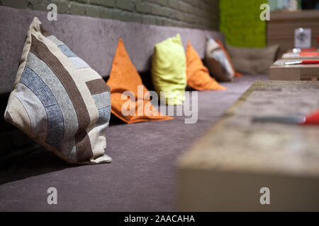 Group of modern brown, green, blue checkered pattern colors fabric pillows on purple cushion clothing sofa and the wall with yellow lights from behind Stock Photo