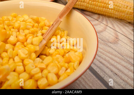 Grains of sweet corn in a plate with a wooden spoon and ears of corn on the table. Healthy diet. Fitness diet. For a sweet treat. Close up Stock Photo