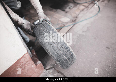 Shallow depth of field (selective focus) image with a mechanic changing the regular summer tyres of a car with winter tyres in a dirty car service. Stock Photo