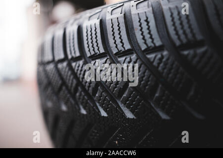 Shallow depth of field (selective focus) image with details of a dirty winter tyre in a car workshop. Sipes and cuts in the tread highlighted. Stock Photo