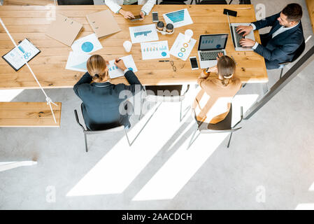 Business people working with computers and some printed statistics at the wooden table in the meeting room, view from the above with copy space Stock Photo