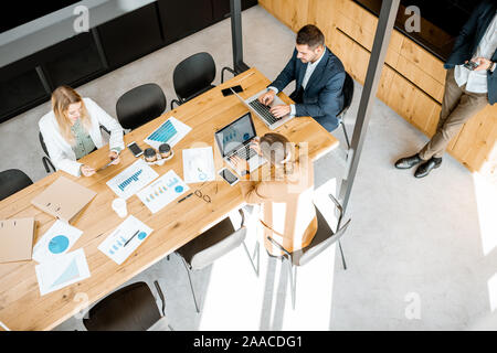 Business people working with computers and some printed statistics at the wooden table in the meeting room, view from the above Stock Photo