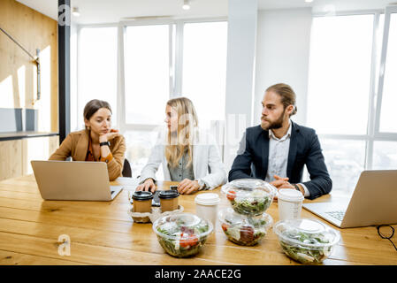 Office workers sitting in the office with business lunches on the foreground. Concept of healthy takeaway food on the work Stock Photo
