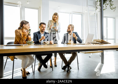 Group of a young office workers eating salads and drinking coffee at the modern office canteen. Concept of a healthy takeaway food on the work Stock Photo