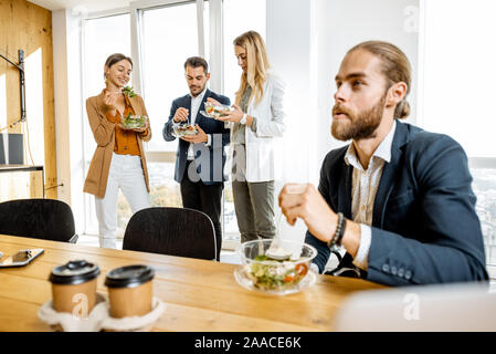 Group of a young office workers eating salads and drinking coffee at the modern office canteen. Concept of a healthy takeaway food on the work Stock Photo