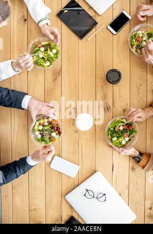 Office workers during a business lunch with healthy salads and coffee cups, view from above on the wooden table Stock Photo