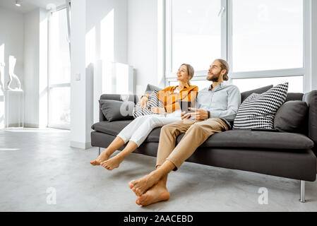 Happy young couple sitting together on the couch in the bright living room of the modern apartment, enjoying their new home Stock Photo