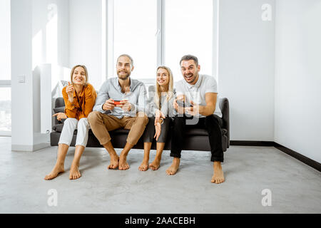 Group of a young friends having fun while playing video games on the couch at home. Concept of leisure and video games at home Stock Photo